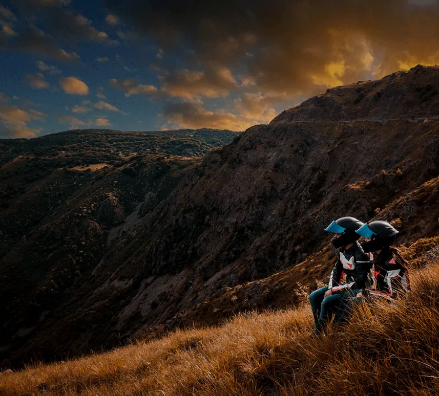 A rider and motorcycle on a grassy hillside at sunset